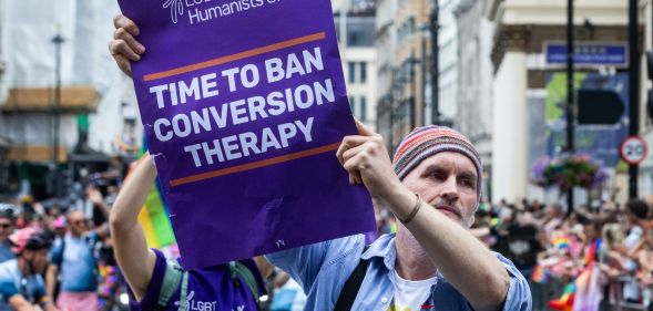 A protestor holds a sign reading "time to ban conversion therapy."