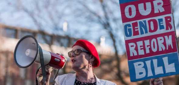 Activist Sarah Jane Baker holds a sign reading "where's our gender reform bill?" and speaks into a bullhorn