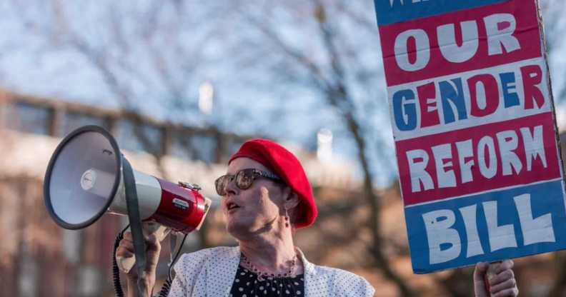 Activist Sarah Jane Baker holds a sign reading "where's our gender reform bill?" and speaks into a bullhorn