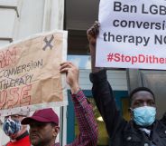 Two people stand side by side and hold up signs during an LGBTQ+ rights protest to ban conversion therapy.