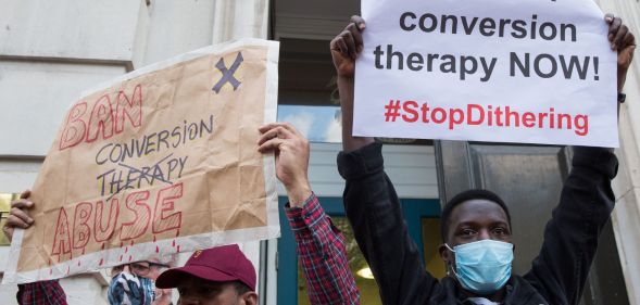 Two people stand side by side and hold up signs during an LGBTQ+ rights protest to ban conversion therapy.