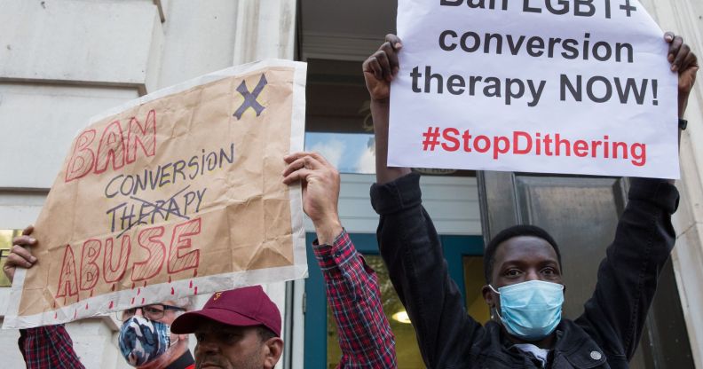 Two people stand side by side and hold up signs during an LGBTQ+ rights protest to ban conversion therapy.